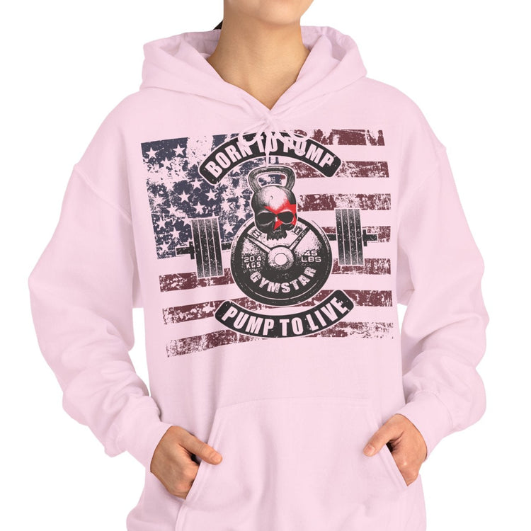 A woman modeling a light pink pullover hoodie with a large front graphic featuring a skull, barbell, American flag elements, and the words 'Rock the Pump Pump to Live' on a plain white background.