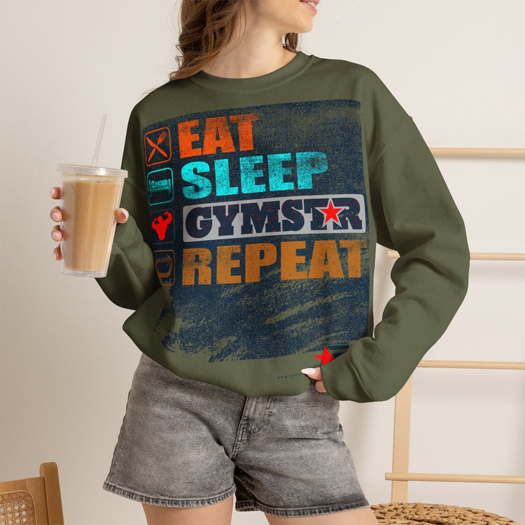 A woman wearing an olive green crewneck sweatshirt with a colorful graphic that reads 'EAT SLEEP GYMSTAR REPEAT' in orange, blue, and white, paired with gray denim shorts and holding a iced coffee.