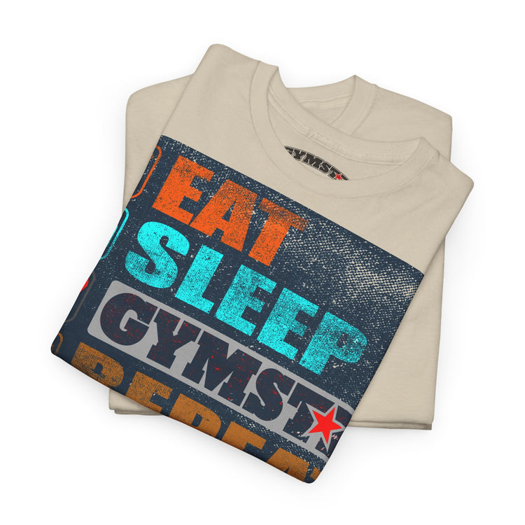 A folded beige t-shirt with a colorful graphic print reading 'EAT SLEEP GYMST' in orange, teal, and dark gray text over a distressed dark blue background, shown on a white background.