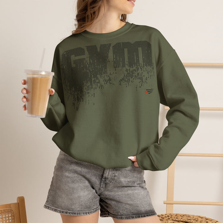 A woman wearing an olive green crewneck sweatshirt with a black distressed 'GYM' graphic on the front, paired with gray denim shorts and holding an iced coffee.