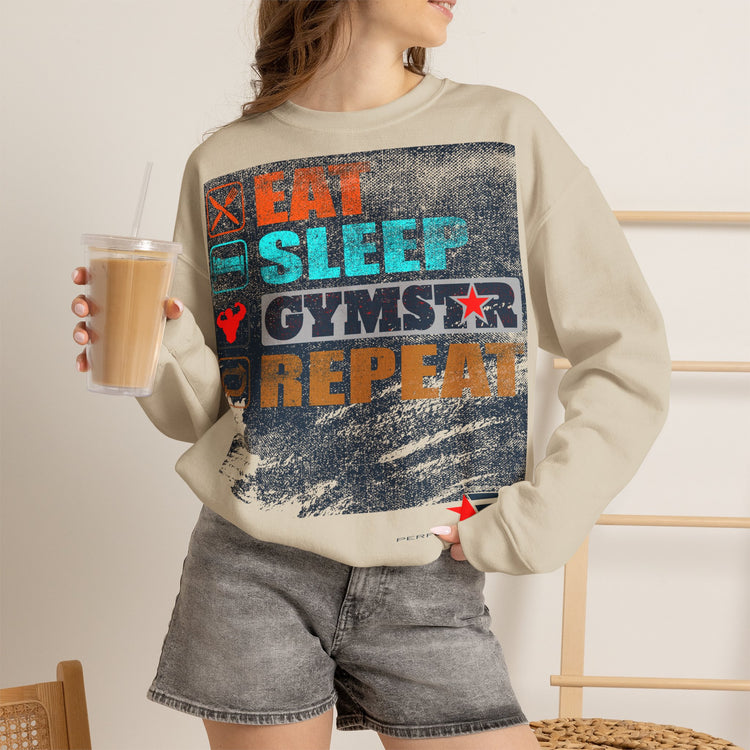 A woman wearing a beige sweatshirt with a large distressed graphic that reads 'EAT SLEEP GYMSTAR REPEAT' in orange, blue, and white, paired with gray denim shorts and holding an iced coffee.