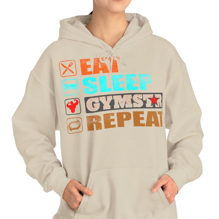 A woman modeling a light beige hoodie with a colorful graphic print that reads 'EAT SLEEP GYMSTAR REPEAT' with small icons, set against a plain white background.