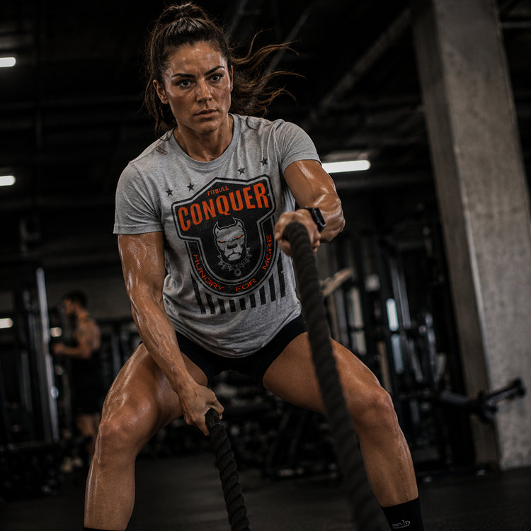 Woman exercising with ropes in a gym wearing a grey Fitbull 'Conquer' t-shirt.