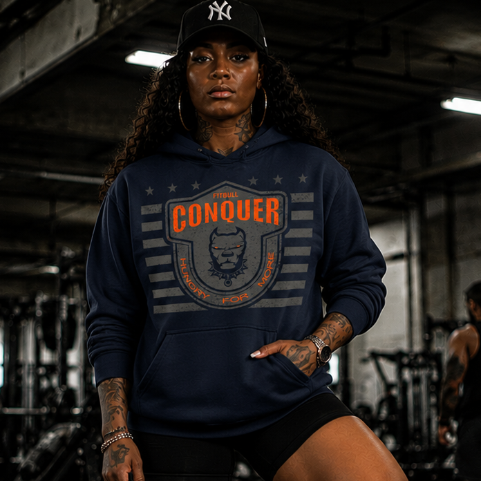 Person wearing a Fitbull navy hoodie with 'Conquer' logo in a gym setting