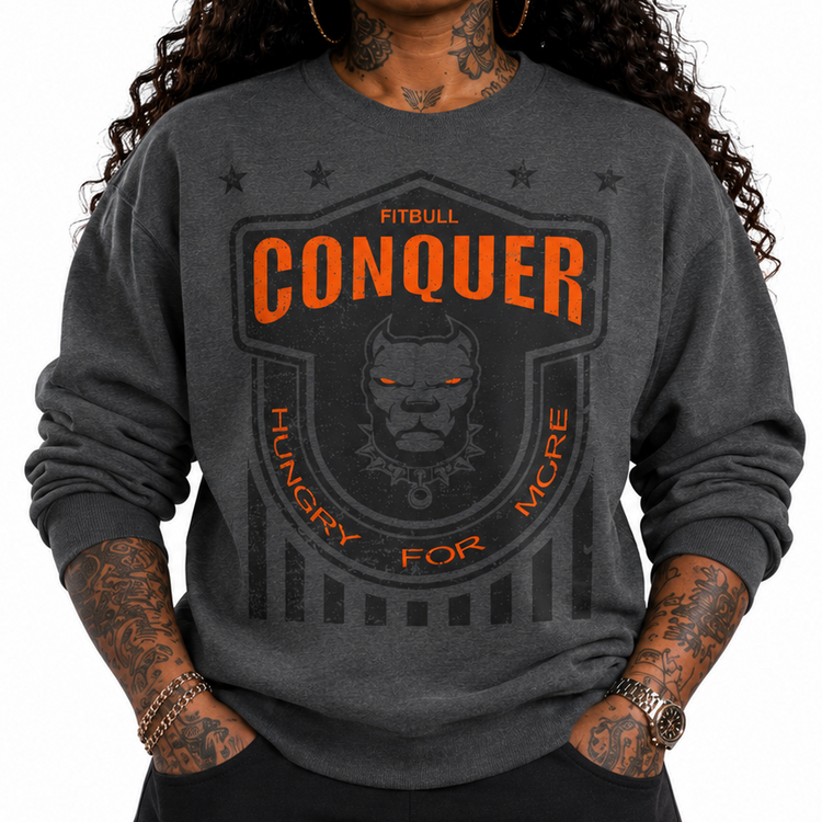 Person wearing a dark gray Fitbull sweatshirt with 'Conquer' logo and text, black cap, and tattoos.