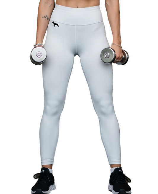 Woman in a gym wearing a white athletic Fitbull leggings outfit and holding dumbbells.