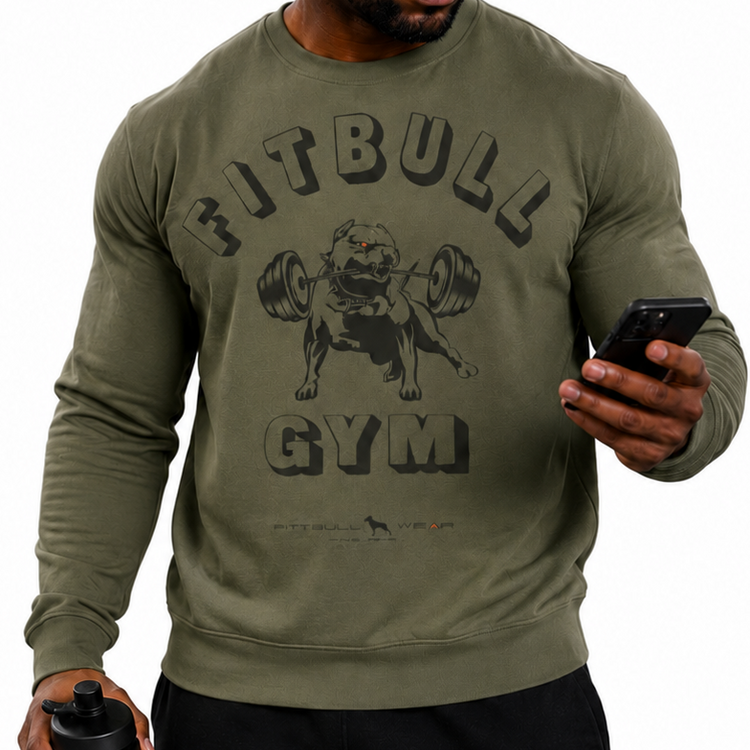 Muscular Black male athlete wearing an olive green FITBULL graphic sweatshirt, black joggers, black FB cap, and dark sunglasses, standing on a clean white studio background. He holds a black FITBULL shaker bottle in one hand and a smartphone in the other, creating a modern fitness lifestyle look. Sportswear streetwear outfit for gym training, bodybuilding, fitness, athleisure, and urban activewear fashion.