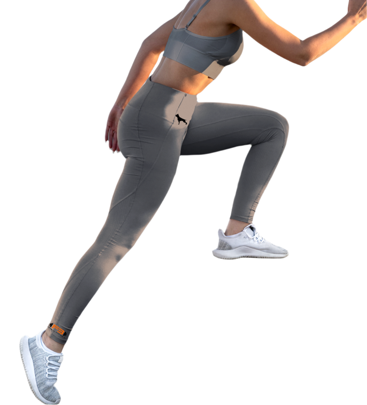 Eine Frau in grauen Fitness-Leggings und einem grauen Fitbull-BH, Frontansicht, macht eine Beinübung