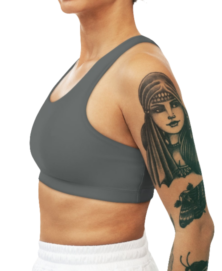 A women's solid gray athletic sports bra Gymsatr, shown from the side. It has a scoop neckline and a racerback style. The sports bra is worn by a person with tattoos on their upper arm.
