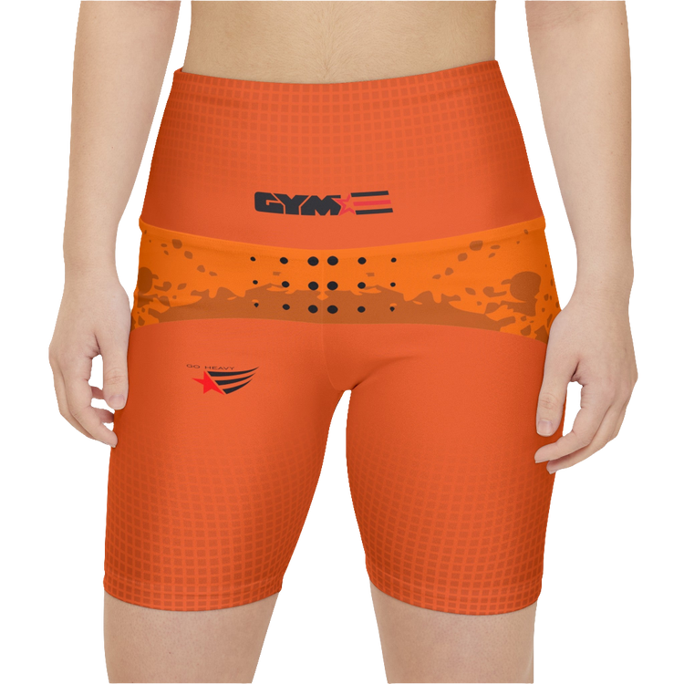 A female fitness model wearing a pair of orange Gymstar workout shorts with black stitching and a Gymstar logo on the upper left thigh area. Front close up view.