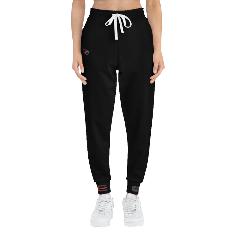 A person standing frontal, wearing black joggers Gymstar with a logoand white sneakers. The joggers have a ribbed bottom and waistband cuffs, and feature two side pockets.