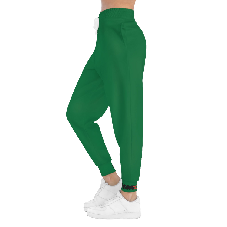 A woman wearing green sports joggers with an elastic waistband and drawstrings, featuring a logo on the left leg and a white sneaker left side view.