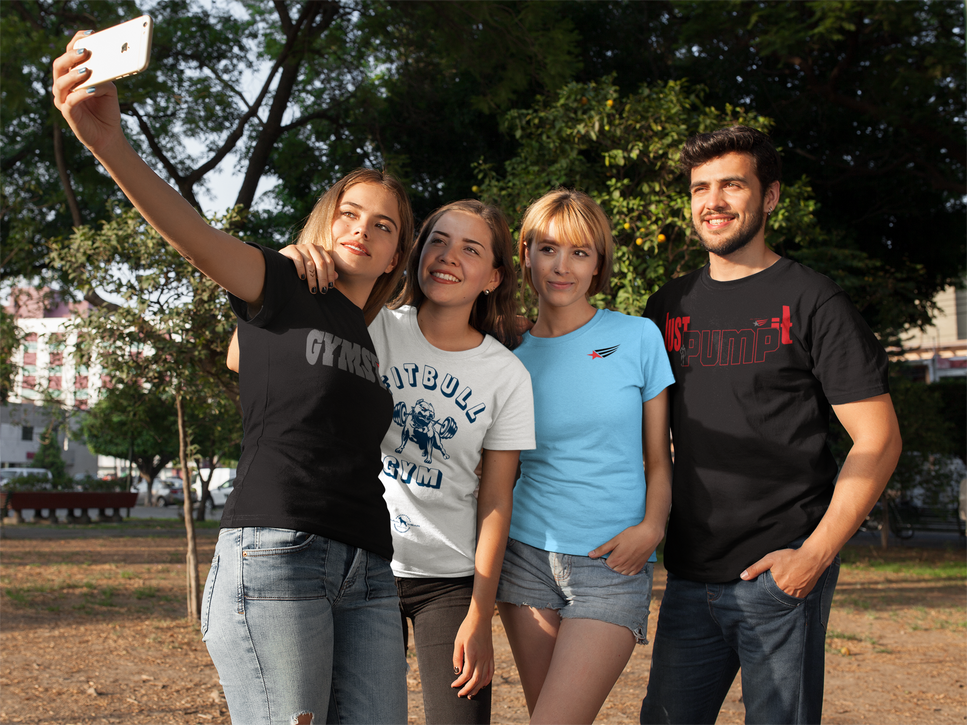 Three girls wearing Massalegents T-shirts and a man wearing a Gymstar T-shirt pose for a selfie on a fitness area in a park.