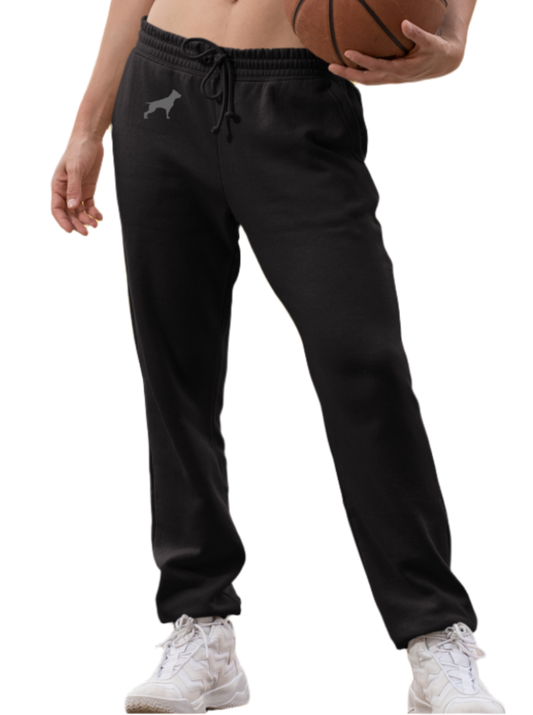 Eine Frau trägt schwarze Fitbull-Jogginghosen mit dem Logo der Marke und ein sportliches kariertes Tanktop. Sie hält einen Basketball.