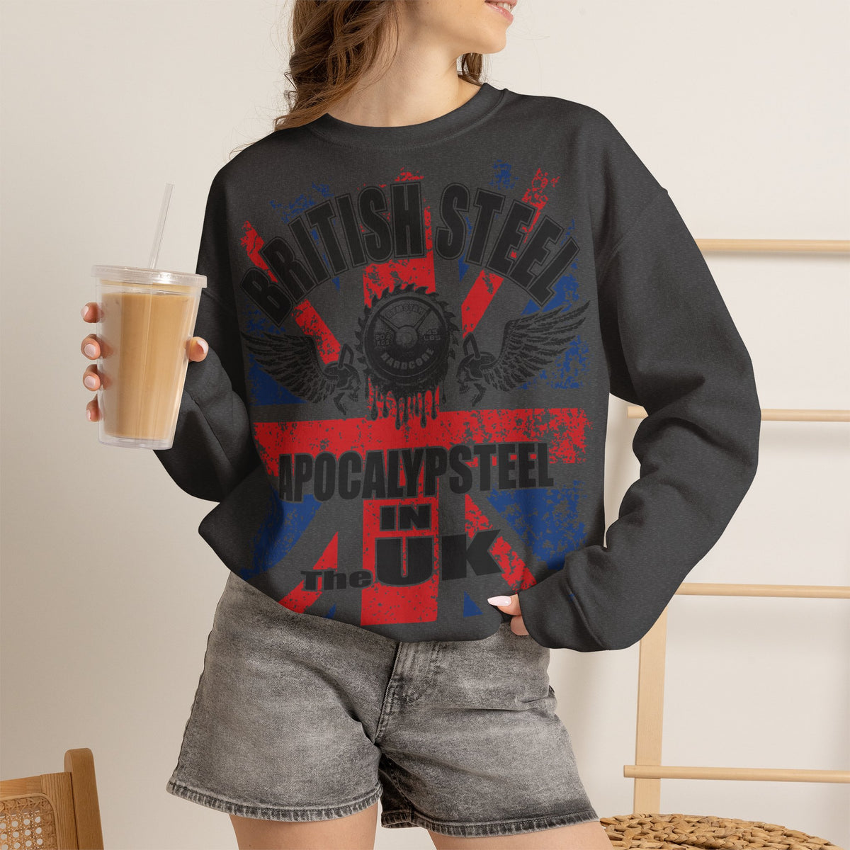 A woman wearing a dark charcoal gray sweatshirt with a 'Southland Rebels' graphic in red and blue, paired with gray denim shorts and holding an iced coffee.