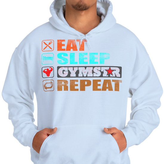 A man wearing a light blue hoodie with a graphic print that reads 'EAT SLEEP GYMSTAR REPEAT' in orange, blue, black, and white, paired with blue jeans against a plain white background.