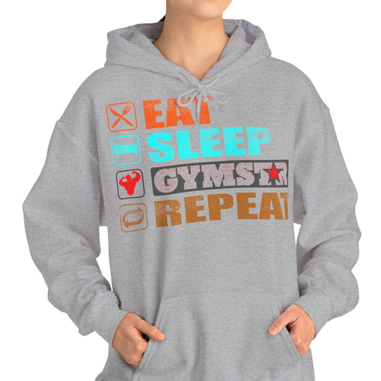 A woman modeling a light gray heather pullover hoodie with a colorful graphic text design on the front that reads 'EAT SLEEP GYMSTAR REPEAT' with small fitness icons, against a plain white background.