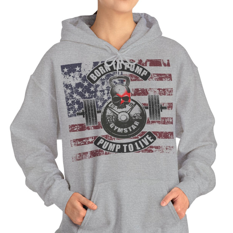 A woman modeling a light gray pullover hoodie with a distressed American flag and weightlifting graphic on the front. The graphic features a skull, barbell, and the text 'Rock The Gym Pump To Live'.