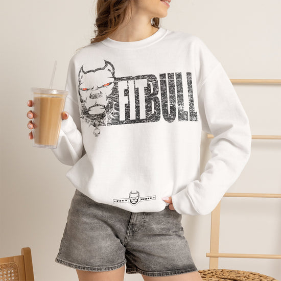 Person wearing a white Fitbull sweatshirt with a graphic design and text, holding a drink.