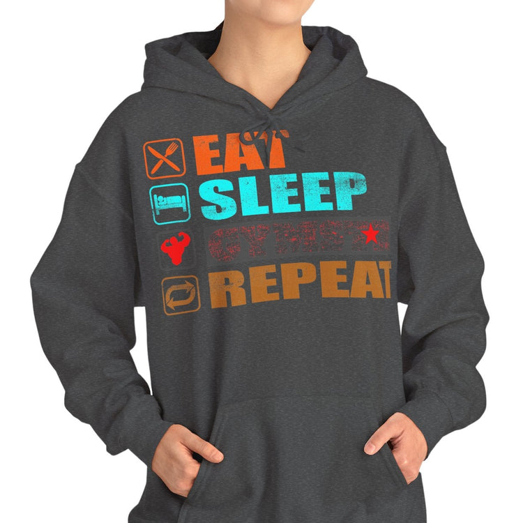 A woman modeling a dark gray pullover hoodie with a colorful graphic on the chest that reads 'EAT SLEEP GYMSTAR REPEAT' with small icons, against a plain white background.