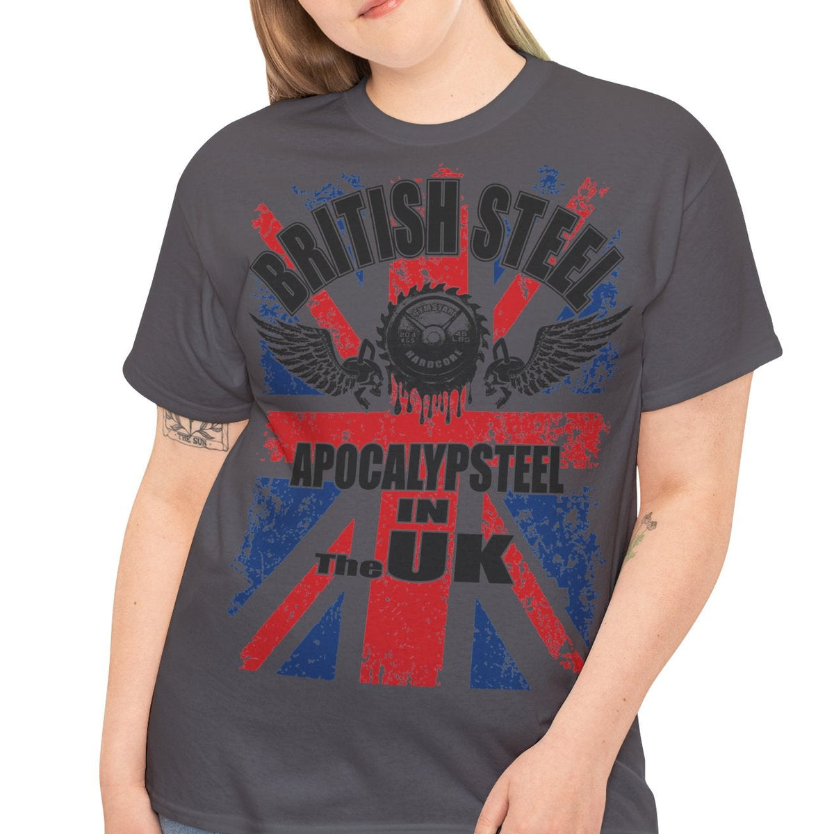 A woman modeling a dark gray graphic t-shirt with a distressed Union Jack design in red and blue, featuring the text 'BRITISH STEEL' and 'APOCALYPSTEEL IN THE UK'.