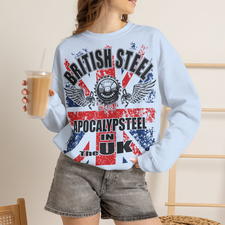 A woman wearing a light blue crewneck sweatshirt with a distressed red, white, and blue graphic that reads 'BRITISH STEEL APOCALYPSTEEL IN THE UK' over a Union Jack design. She is holding a iced coffee and wearing gray denim shorts.