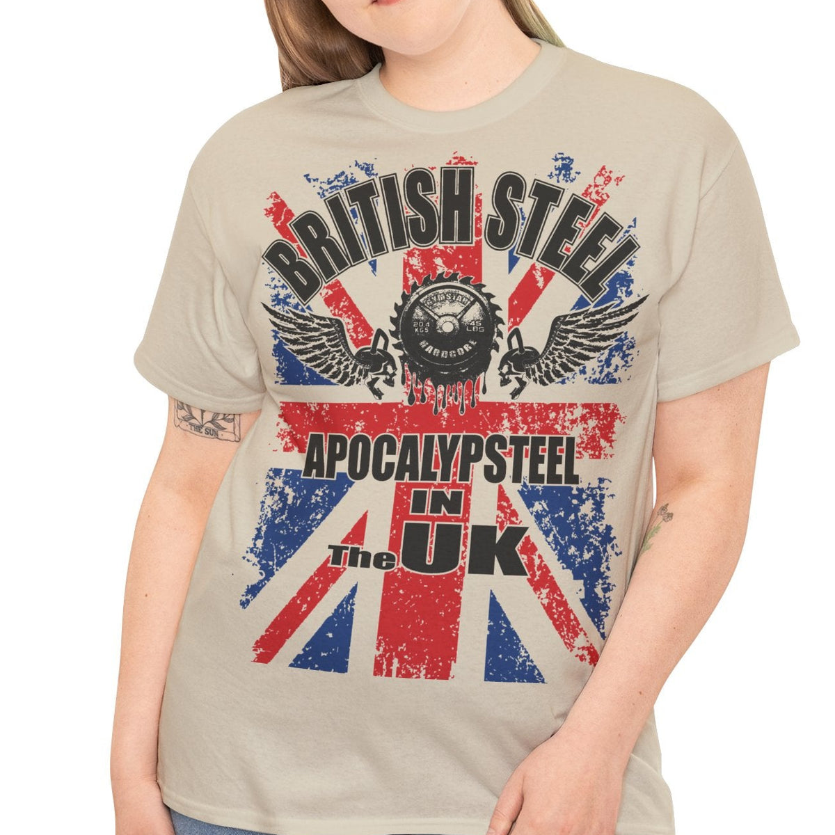 A woman modeling a beige graphic t-shirt with a distressed Union Jack design and the text 'BRITISH STEEL' and 'APOCALYPSTER! IN THE UK'.