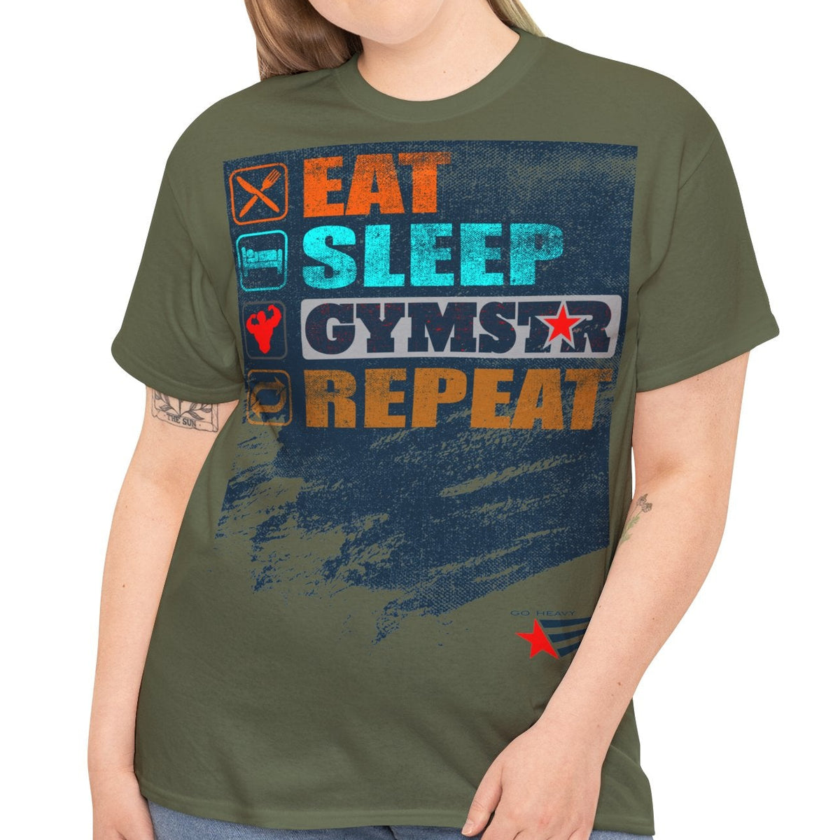 A woman modeling an olive green graphic t-shirt with a distressed blue, orange, and white print that reads 'EAT SLEEP GYMSTAR REPEAT'. She is wearing blue jeans against a plain white background.