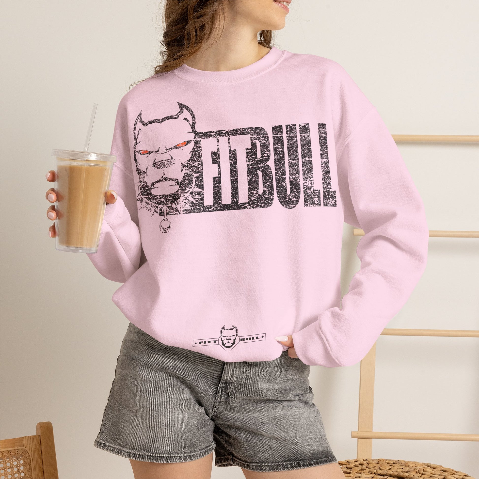 Person wearing a pink sweatshirt with 'Fitbull' logo holding a drink.