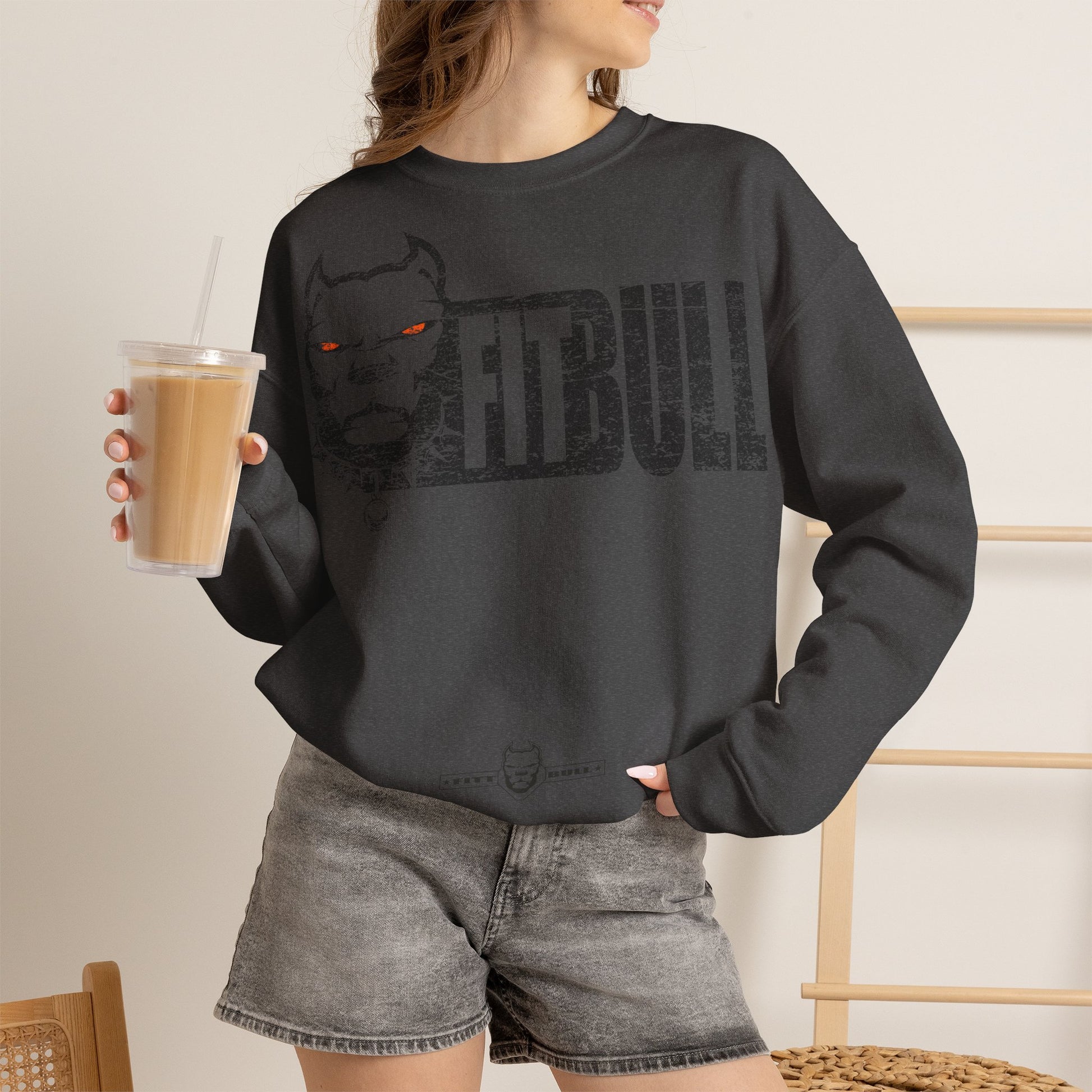 Person wearing a black Fitbull sweatshirt with a nebula design and text, holding a drink.