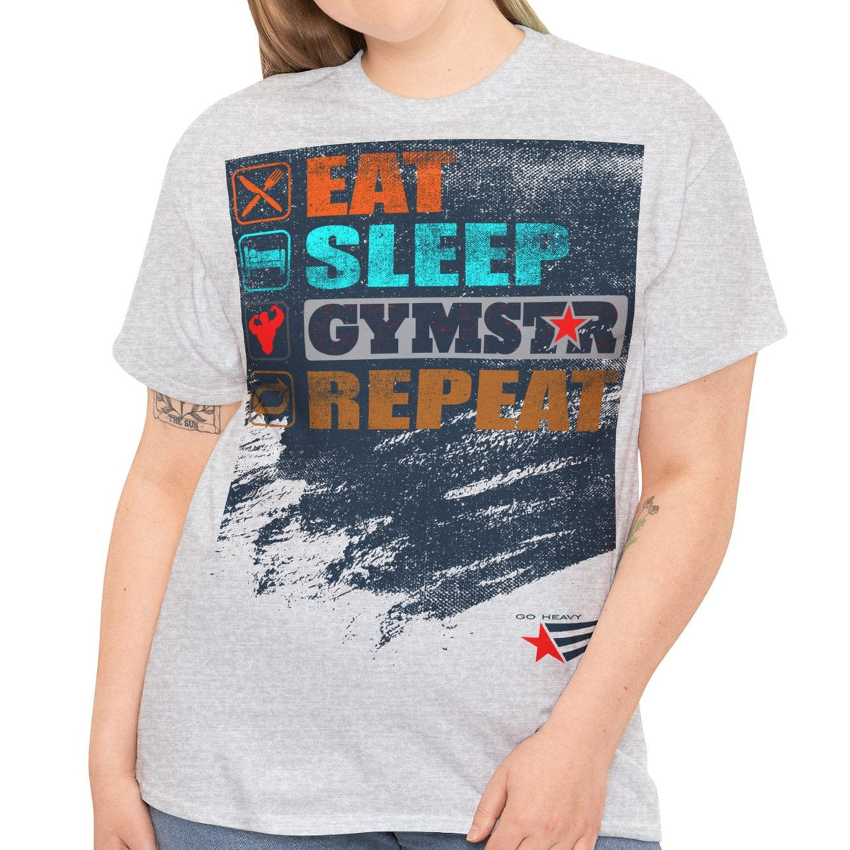 A woman modeling a light heather gray graphic t-shirt with a colorful distressed print that reads 'EAT SLEEP GYMSTAR REPEAT' and a small red star logo near the bottom right, paired with blue jeans against a plain white background.