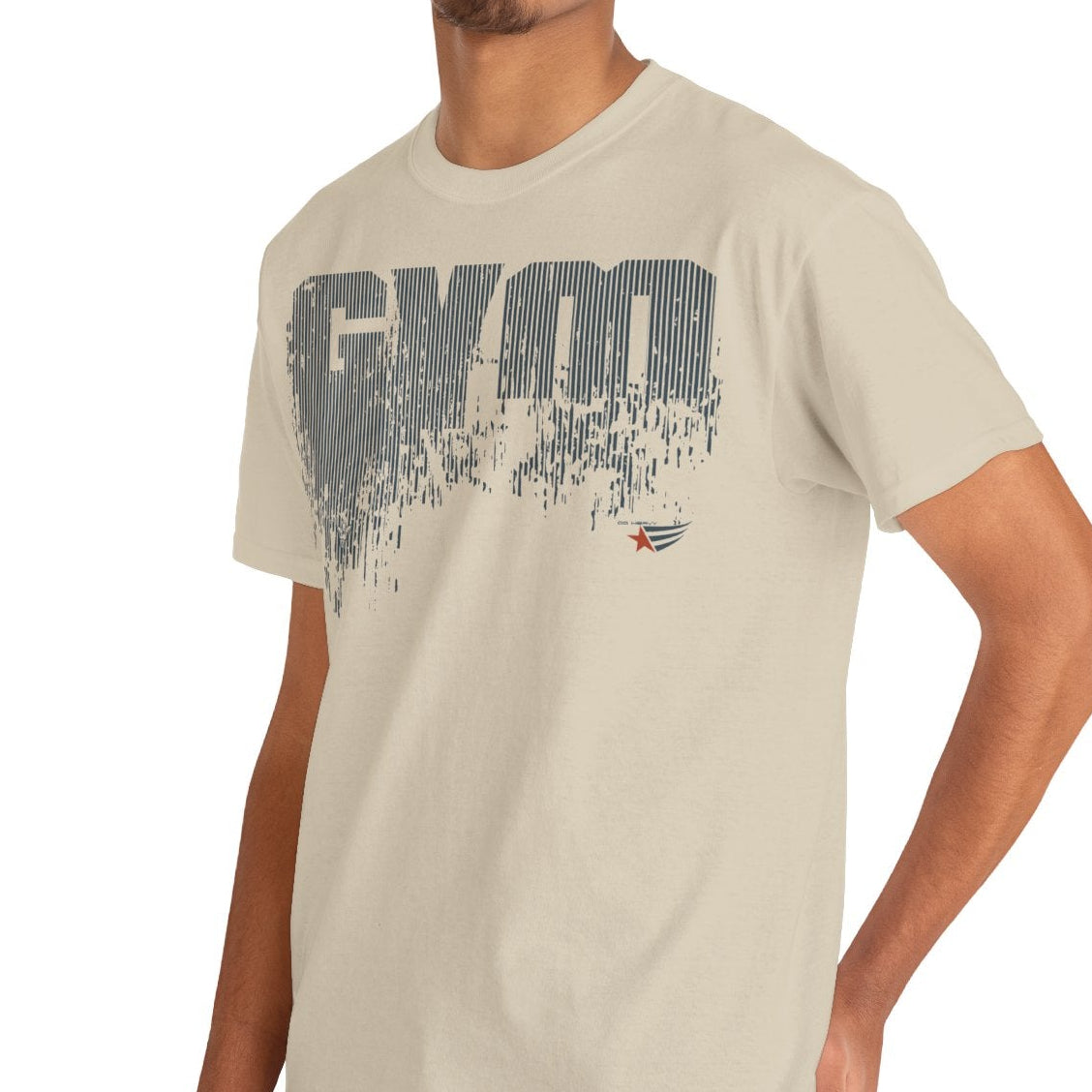 A man wearing a light beige crewneck t-shirt with a distressed gray 'GYM' graphic on the chest, paired with blue jeans, photographed against a solid white background.