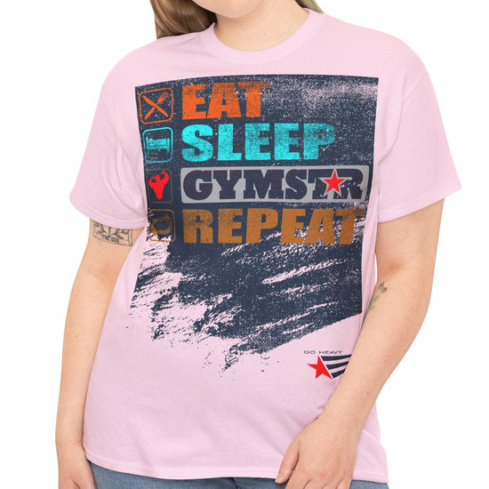 A woman modeling a light pink graphic t-shirt with a distressed design that reads 'EAT SLEEP GYMSTAR REPEAT' in colorful block letters over a dark paint-splatter background. She is wearing blue jeans against a plain white studio background.