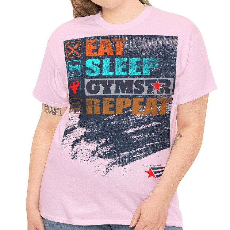 A woman modeling a light pink graphic t-shirt with a distressed design that reads 'EAT SLEEP GYMSTAR REPEAT' in colorful block letters over a dark paint-splatter background. She is wearing blue jeans against a plain white studio background.