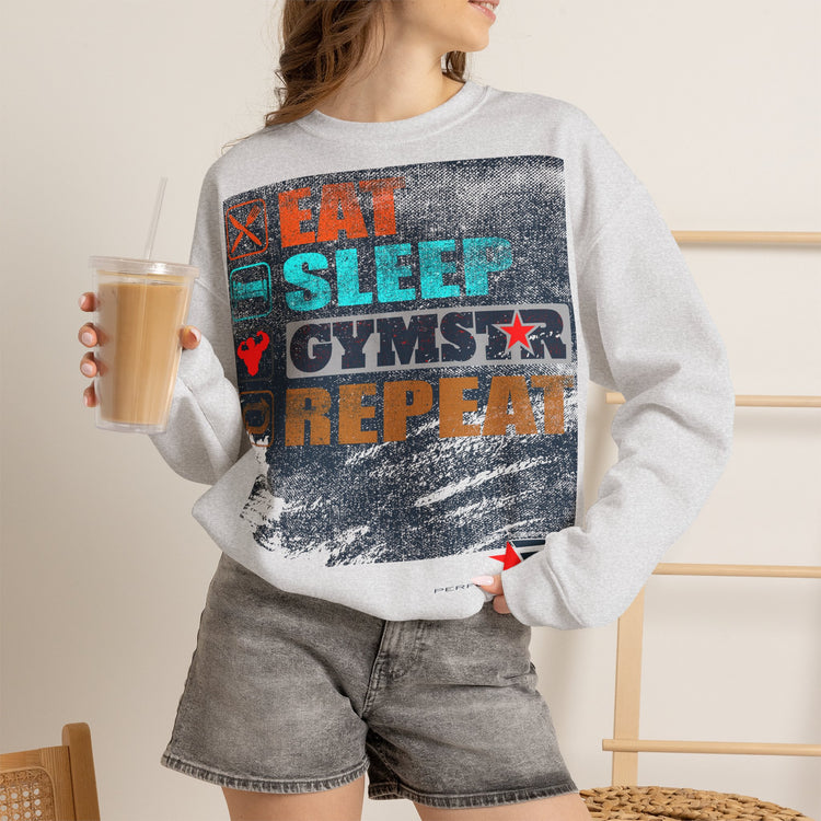 A woman wearing a light gray sweatshirt with a large distressed graphic that reads 'EAT SLEEP GYMSTAR REPEAT' in orange, teal, and dark blue, paired with gray denim shorts and holding a drink.