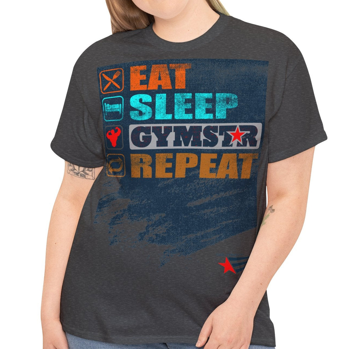 A woman modeling a dark charcoal gray graphic t-shirt with the words 'EAT SLEEP GYMSTAR REPEAT' in colorful block letters, paired with blue jeans, against a plain white background.