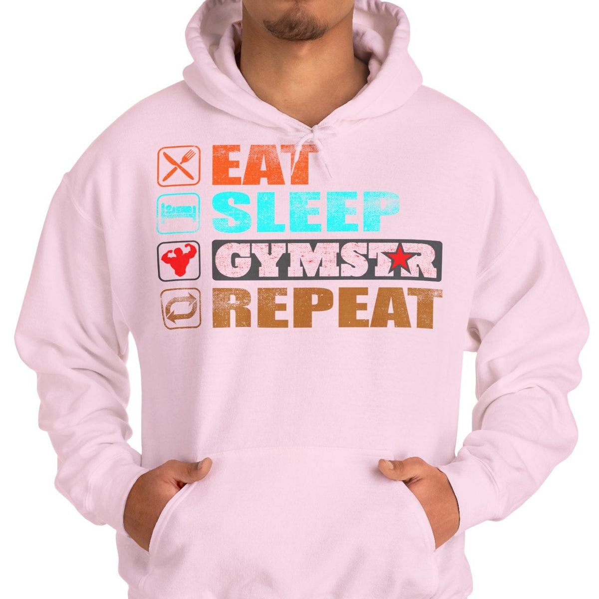 A man wearing a light pink pullover hoodie with a colorful graphic on the chest that reads 'EAT SLEEP GYMSTAR REPEAT' with small icons, paired with blue jeans, against a plain white background.