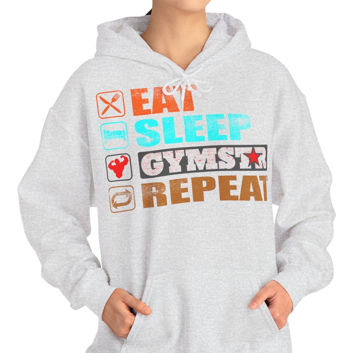 A woman modeling a light gray heather hoodie with a colorful graphic text design that reads 'EAT SLEEP GYMSTX REPEAT' with small icons, set against a plain white background.