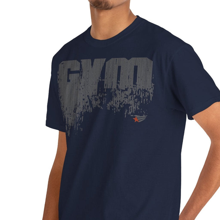 A man wearing a navy blue crewneck t-shirt with a distressed gray 'GYM' graphic on the chest, paired with blue jeans, photographed against a solid white background.