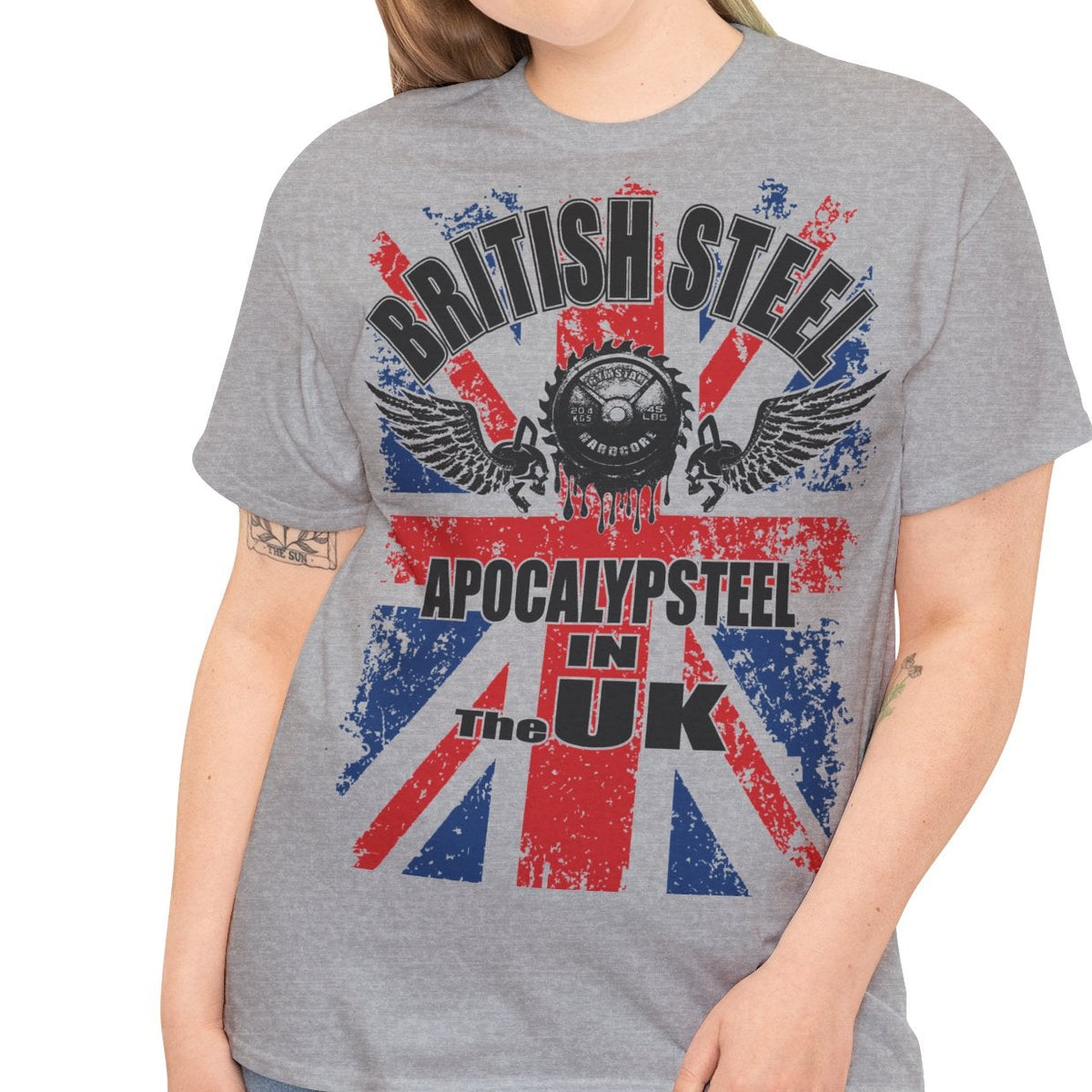 A woman modeling a heather gray graphic t-shirt featuring a distressed Union Jack design with the text 'BRITISH STEEL' and 'APOCALYPSTER! IN THE UK'.