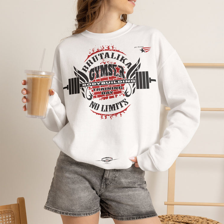 A woman wearing a white crewneck sweatshirt with a red and black gym graphic that reads 'DRUTALIKA GYMSTAR NO LIMITS' and 'BODYBUILDING TRAINING AWARD', paired with gray denim shorts, holding an iced coffee in a cafe setting.