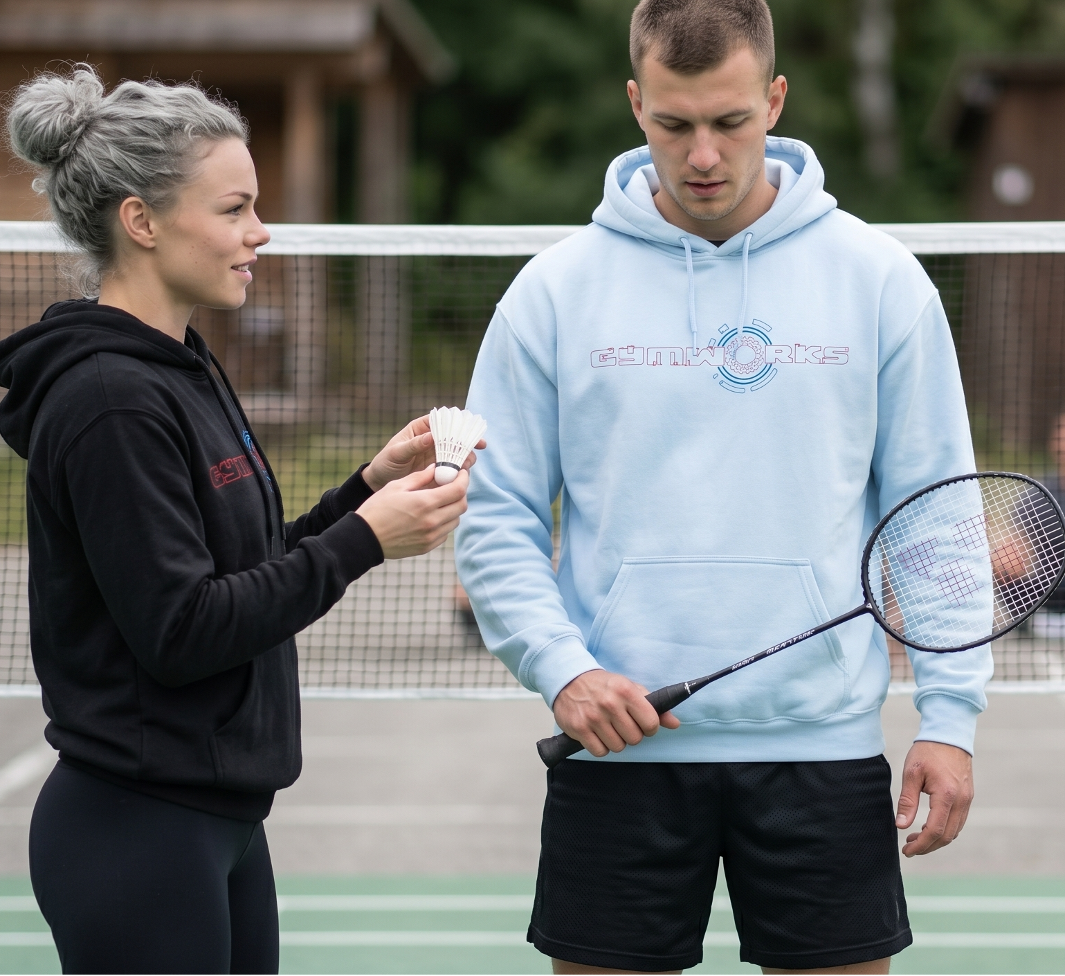 Two people on a badminton court with Gymworks hoodie one holding a racket and the other holding a cup.