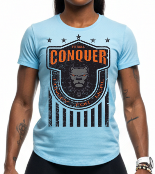 Woman wearing a light blue Fitbull t-shirt with 'Conquer' motivational design printed on it, black leggings, and colorful sneakers.