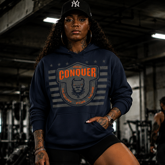 Person wearing a Fitbull navy hoodie with 'Conquer' logo in a gym setting