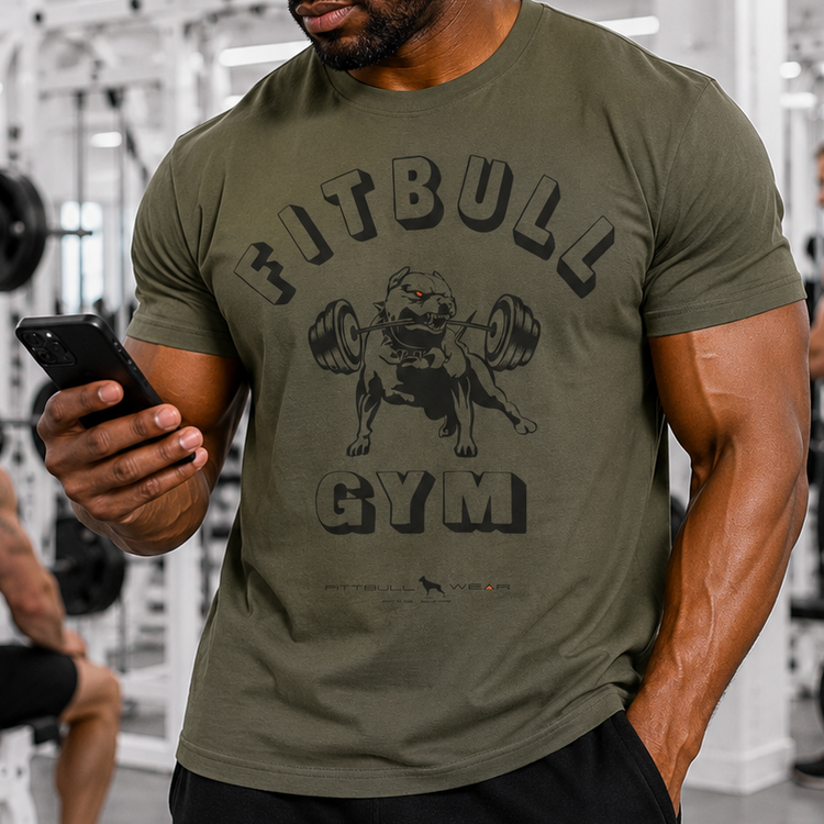 Man in a gym wearing a Fitbull Gym t-shirt and cap, using a phone.