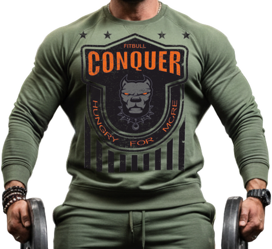 Man in a gym wearing a Fitbull bodybuilding green 'Conquer' sweatshirt and holding weights.