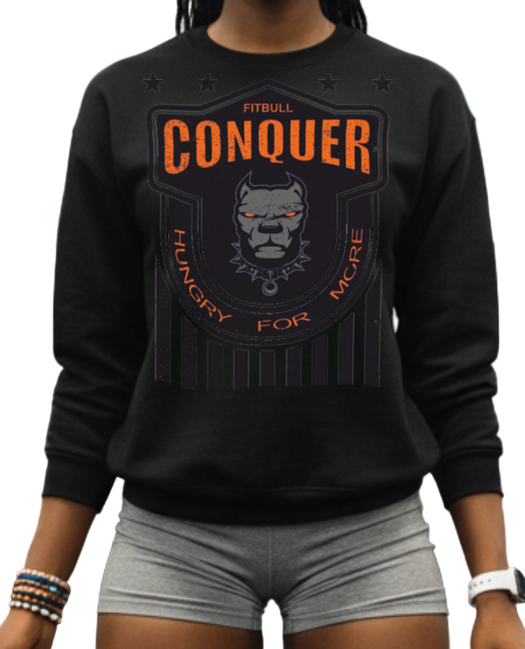 Woman in a gym wearing a Fitbull fitness 'Conquer' sweatshirt, holding a water bottle and jump rope.