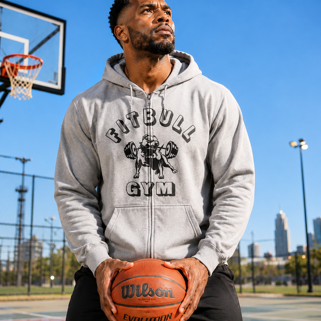 Man holding a basketball on a basketball court wearing a 'FITBULL GYM' hoodie.