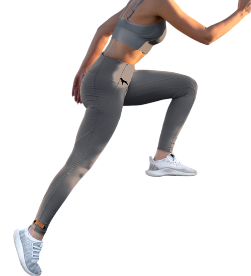 Eine Frau in grauen Fitness-Leggings und einem grauen Fitbull-BH, Frontansicht, macht eine Beinübung
