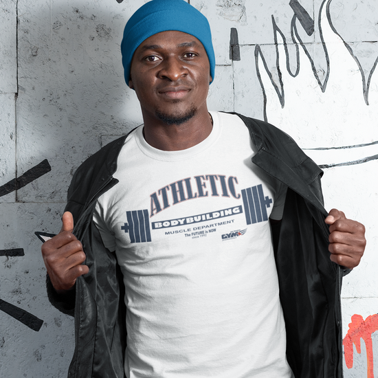 Man wearing a white Gymstar t-shirt with 'Athletic' text, blue beanie, and black jacket in front of a graffiti wall.
